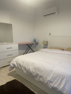 A bedroom with a bed, a dresser, an ironing board, and a lamp. - 2 bedrooms apartment in rehab city (New Cairo)