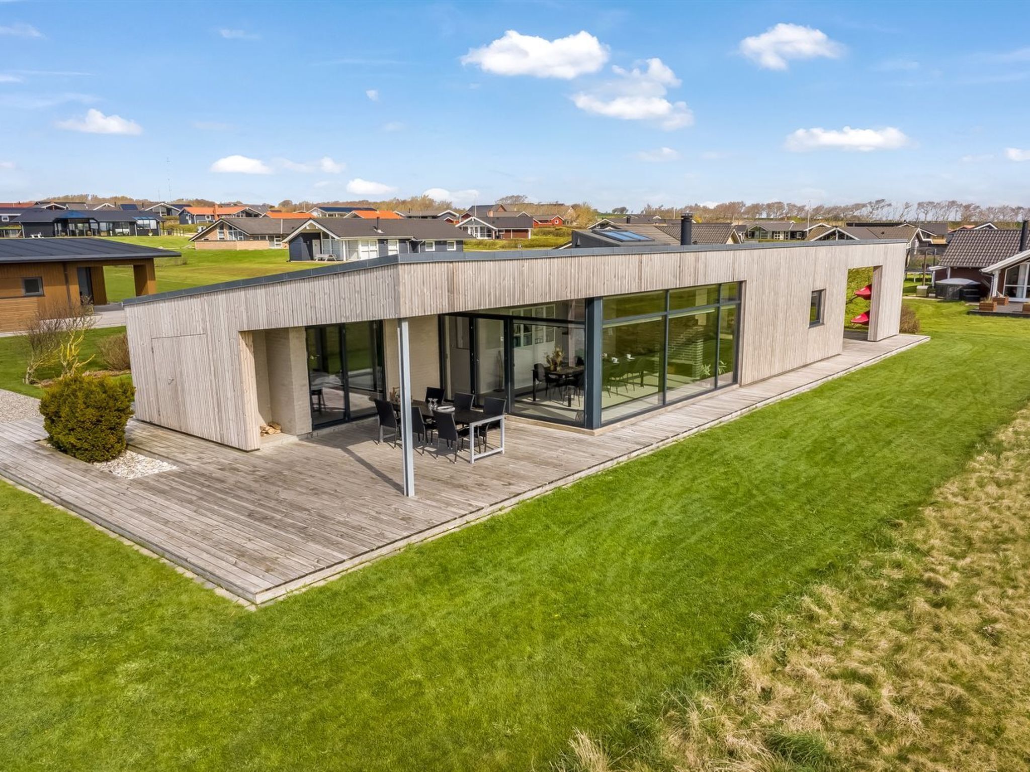 A modern house with a large glass patio, a wooden deck, and a view of neighboring houses.