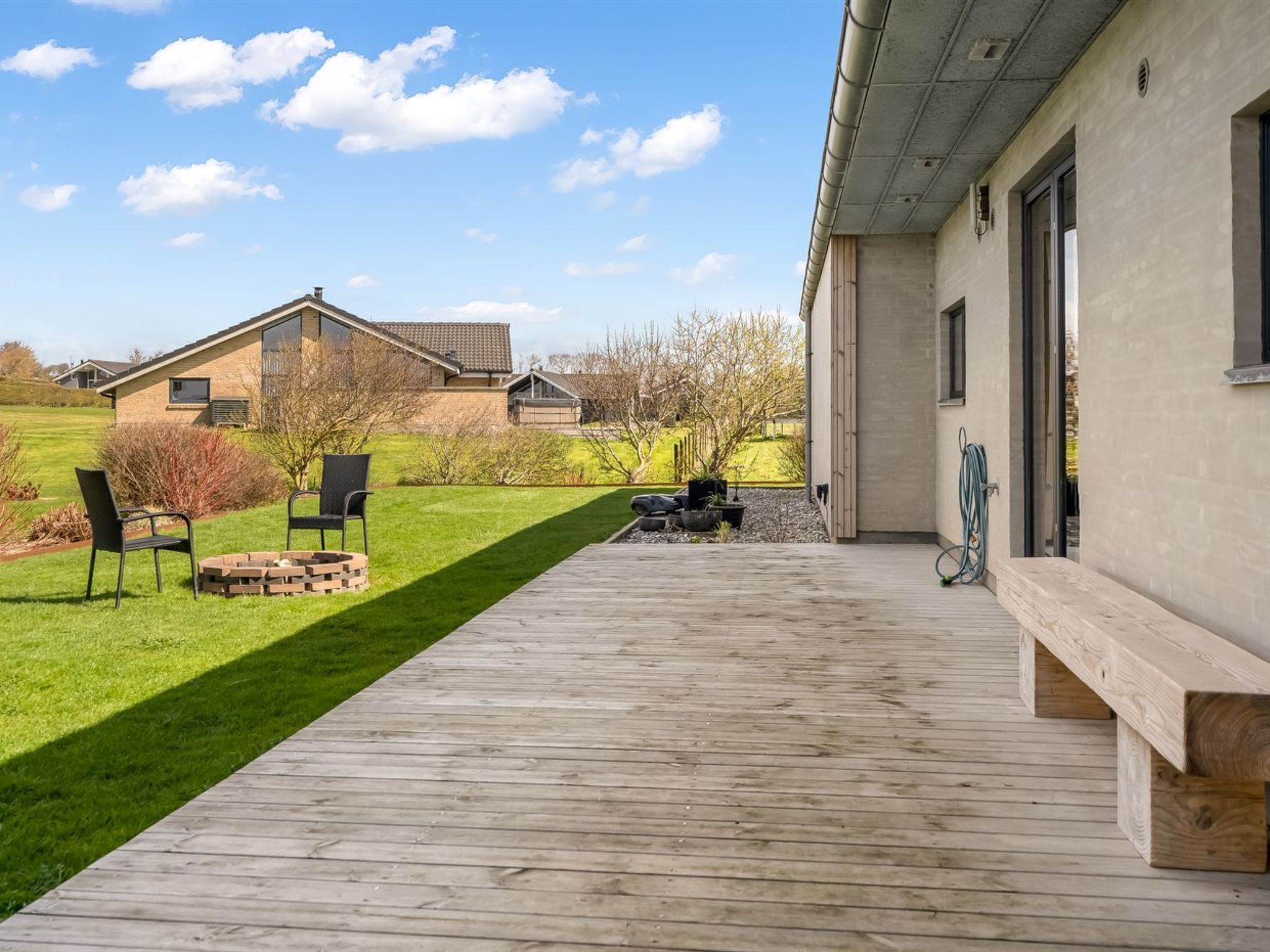 A wooden deck leading to a house with a brick exterior, a grassy yard, and a clear sky.