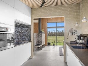 Eine moderne Küche mit Ziegelrückwand, einem großen Fenster und Blick ins Freie.