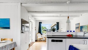 A modern kitchen with white cabinetry, a built-in dishwasher, and a dining area with a table and chairs. - "Tinka" - 100m from the sea by Interhome (Strandby)