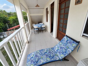 Uma varanda com mesa e cadeiras, uma poltrona de descanso e vista para o verde.
