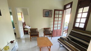 A room with a sofa, two chairs, a wooden table, a bed, a painting, and a window with blinds. - Sainte-Anne | Pointe Marin beach 400m away! (Sainte-Anne)