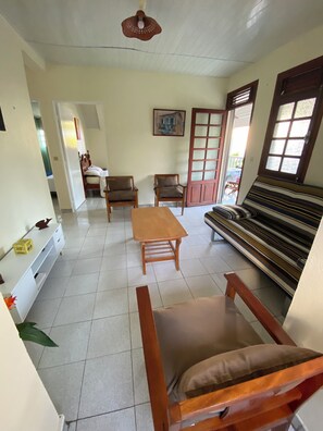 A room with a sofa, two chairs, a wooden table, a bed, a painting, and a window with blinds. - Sainte-Anne | Pointe Marin beach 400m away! (Sainte-Anne)