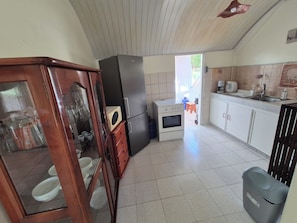 A kitchen with a refrigerator, oven, and microwave. There is a wooden cabinet with glass doors containing bowls. A trash bin is visible in the foreground. - Sainte-Anne | Pointe Marin Beach is 400 meters away! (Sainte-Anne)