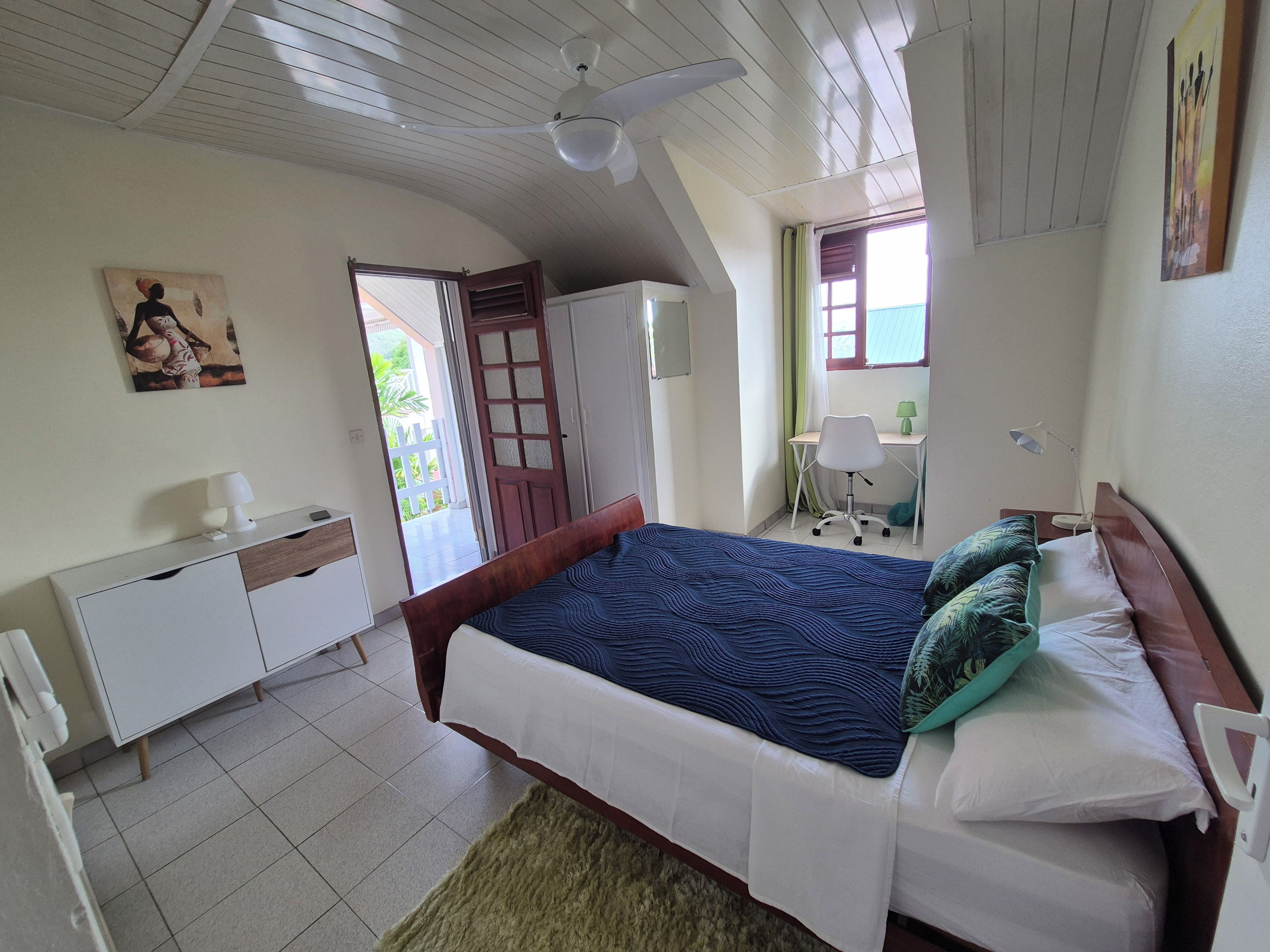 Ein Schlafzimmer mit einem Bett, einem Schreibtisch, einem Sessel, einem Kleiderschrank und einem Deckenventilator.