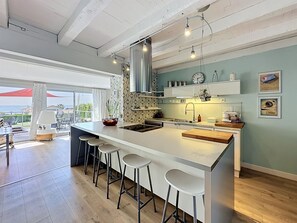A modern kitchen with a large island, bar stools, and a view to the outside. - L'Incroyable Océane by Interhome (Pornic)