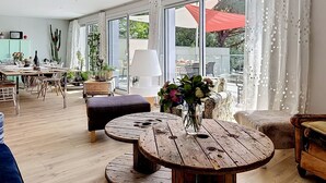 A spacious living area with a large sliding glass door, a round wooden coffee table, and a dining area with a table set for four. - L'Incroyable Océane by Interhome (Pornic)