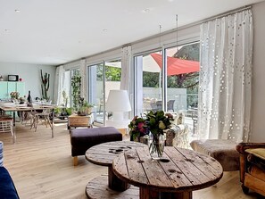 A spacious living area with a large sliding glass door, a round wooden coffee table, and a dining area with a table set for four. - L'Incroyable Océane by Interhome (Pornic)