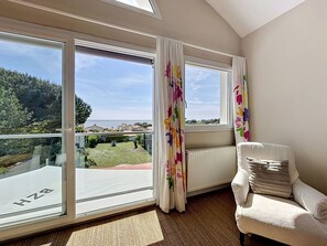 Ein Zimmer mit großen Fenstern, einem Heizkörper, einem weißen Stuhl und Blick auf eine grüne Landschaft.