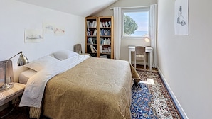 Un dormitorio con cama, escritorio, estantería y ventana con vistas.