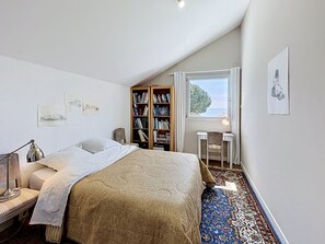 Ein Schlafzimmer mit Bett, Schreibtisch, Bücherregal und einem Fenster mit Blick.