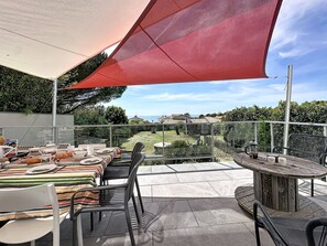Eine Terrasse im Freien mit einem Esstisch, Stühlen und einem runden Tisch mit einem Getränk.