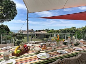 En uteservering med utsikt över havet, ett bord dukat med tallrikar, glas och en fruktskål.