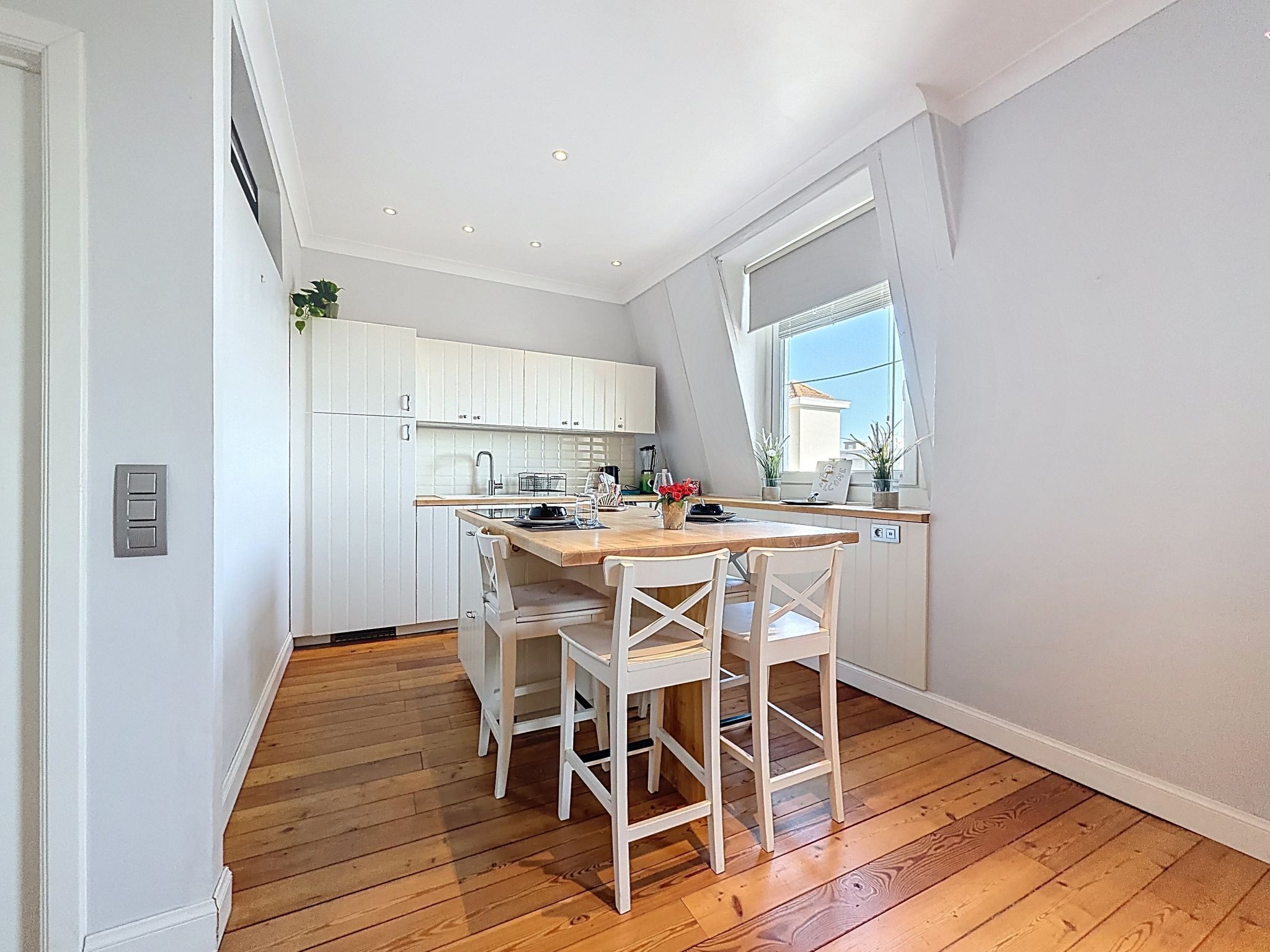 A modern kitchen with white cabinets, a wooden dining table, and a window with a view.