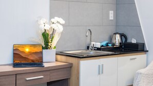 A modern kitchen with a laptop, a sink, a kettle, and a vase of flowers. - Serenity Hotel Near Tan Son Nhat Airport (Ho Chi Minh City)