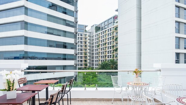 A modern outdoor seating area with tables and chairs, a railing, and a view of high-rise buildings. - Serenity Hotel Near Tan Son Nhat Airport (Ho Chi Minh City)