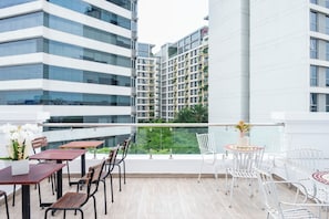 A modern outdoor seating area with tables and chairs, a railing, and a view of high-rise buildings. - Serenity Hotel Near Tan Son Nhat Airport (Tan Son Hoa)