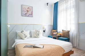 A hotel room with a bed, a side table with fruit, a blue chair, and a wall-mounted lamp. - Serenity Hotel Near Tan Son Nhat Airport (Tan Son Hoa)