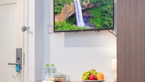 A minibar with a television displaying a waterfall, a plate of fruit, and bottled water. - Serenity Hotel Near Tan Son Nhat Airport (Ho Chi Minh City)