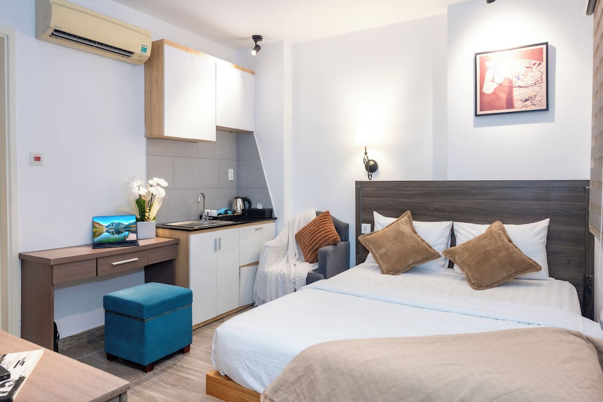 A modern hotel room with a bed, a desk, a kitchenette, and a bathroom.
