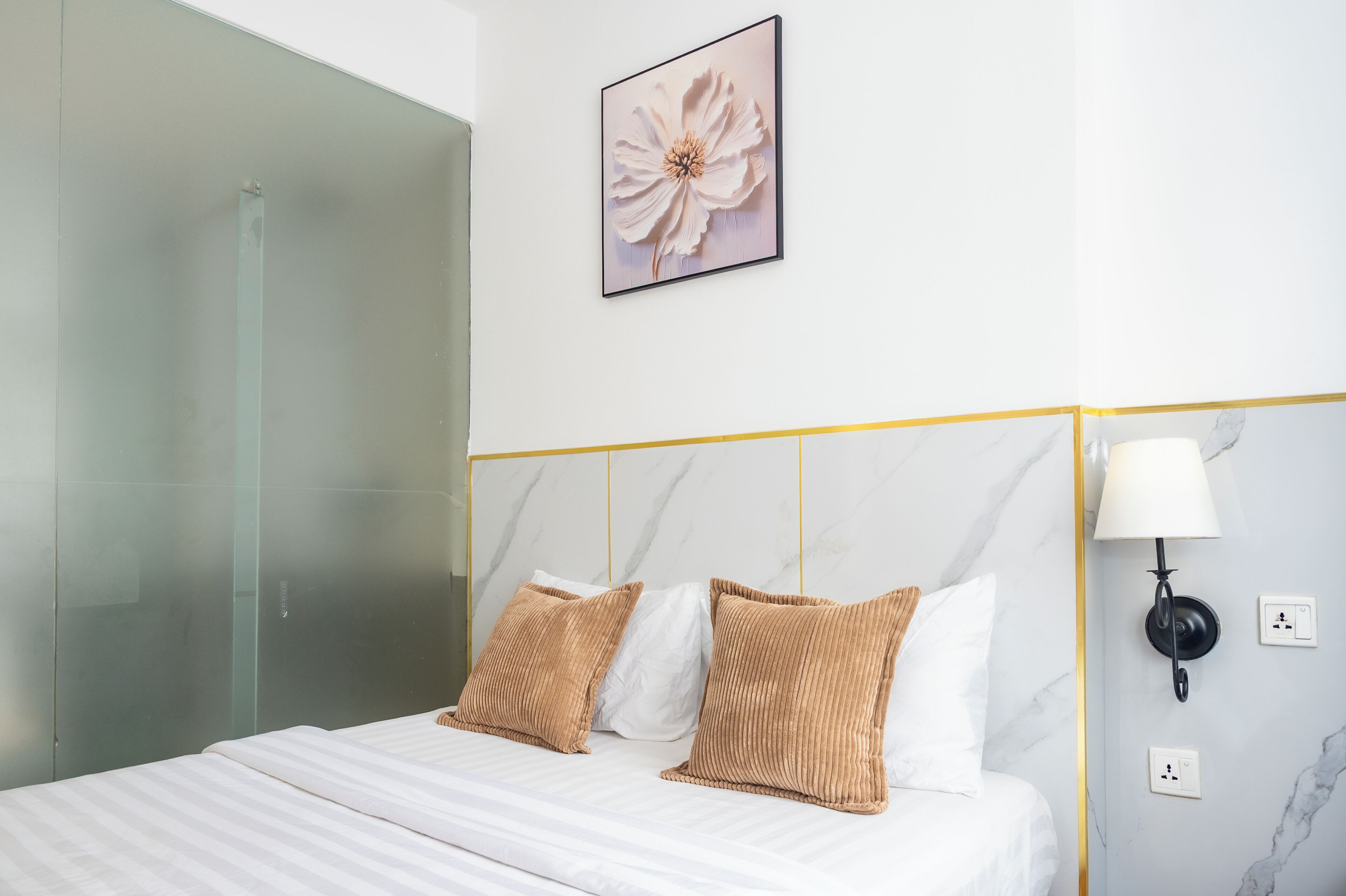 A hotel room with a bed, a glass shower, a marble wall, and a framed picture.