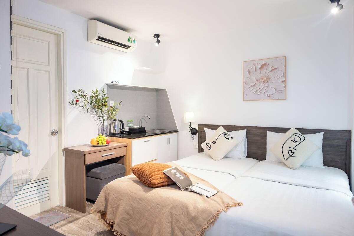 A hotel room with a bed, bedside table, desk, and a wall-mounted air conditioner.