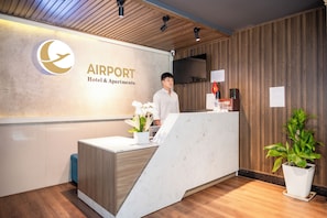 A reception desk with a logo, a man standing behind it, and a potted plant. - Serenity Hotel Near Tan Son Nhat Airport (Tan Son Hoa)