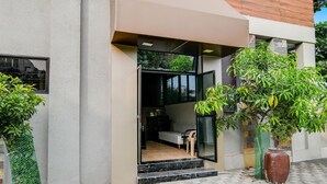 Une entrée moderne avec une porte en verre, un petit espace salon à l’intérieur et des plantes en pot à l’extérieur.
