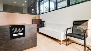 Un comptoir d’accueil portant l’inscription « Collection », un canapé blanc, une chaise noire en tissu ajouré et de grandes fenêtres donnant sur un paysage verdoyant.
