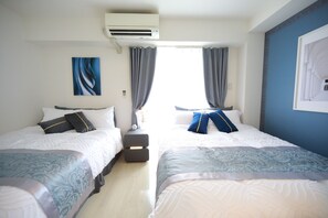A hotel room with two beds, an air conditioning unit, a nightstand with a lamp, and a window with curtains.