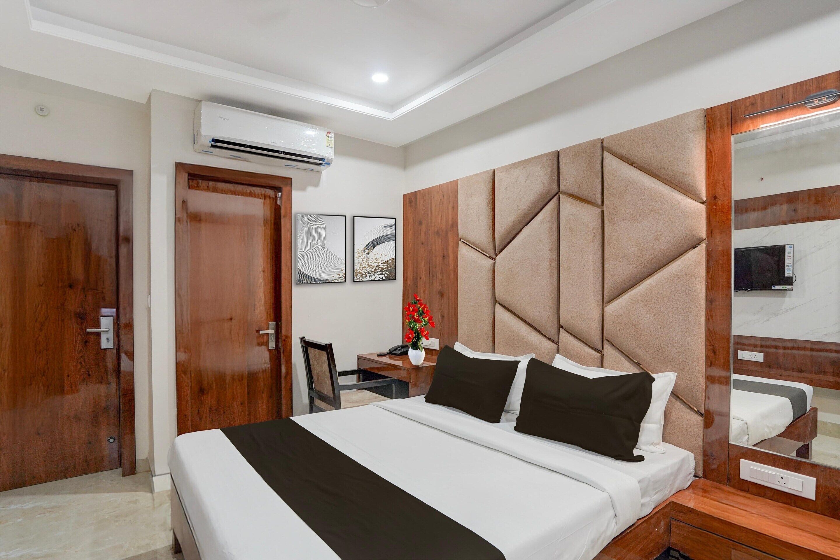 Habitación de hotel con cama, escritorio, silla, aire acondicionado, espejo y puertas de madera.