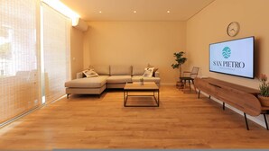 A modern living room with a sectional sofa, a coffee table, a TV mounted on the wall, and a wooden bench. - SanPietro Vacation Apartment 012 (Plazhi San Pietro)