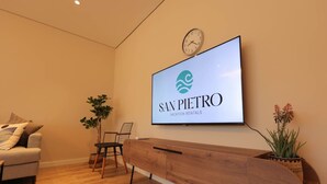 A reception area with a wooden reception desk, a clock, a flat-screen TV displaying 'SAN PIERRO Vacation Rentals,' a sofa, and two potted plants. - SanPietro Vacation Apartment 012 (Plazhi San Pietro)