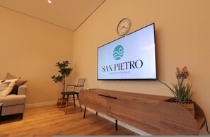 A reception area with a wooden reception desk, a clock, a flat-screen TV displaying 'SAN PIERRO Vacation Rentals,' a sofa, and two potted plants. - SanPietro Vacation Apartment 012 (Plazhi San Pietro)