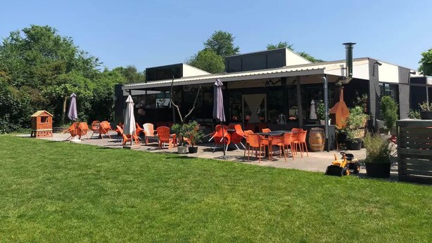 An outdoor seating area with orange chairs and tables, a small playhouse, and a building with a chimney. - Vacation home near the North Sea and forest. Bergen, NH, Schoorl, Schoorldam (Warmenhuizen)