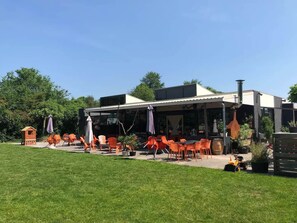 An outdoor seating area with orange chairs and tables, a small playhouse, and a building with a chimney.