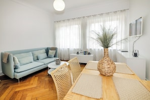 A living room with a sofa, chairs, a coffee table, a dining table with placemats, a vase, and a television on the wall. - Haus Spiegel - Blue Heaven vacation apartment (Lindau (Bodensee))