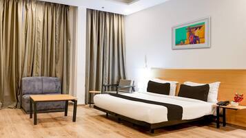 A hotel room with a bed, a desk, a chair, a sofa, and a painting on the wall.
