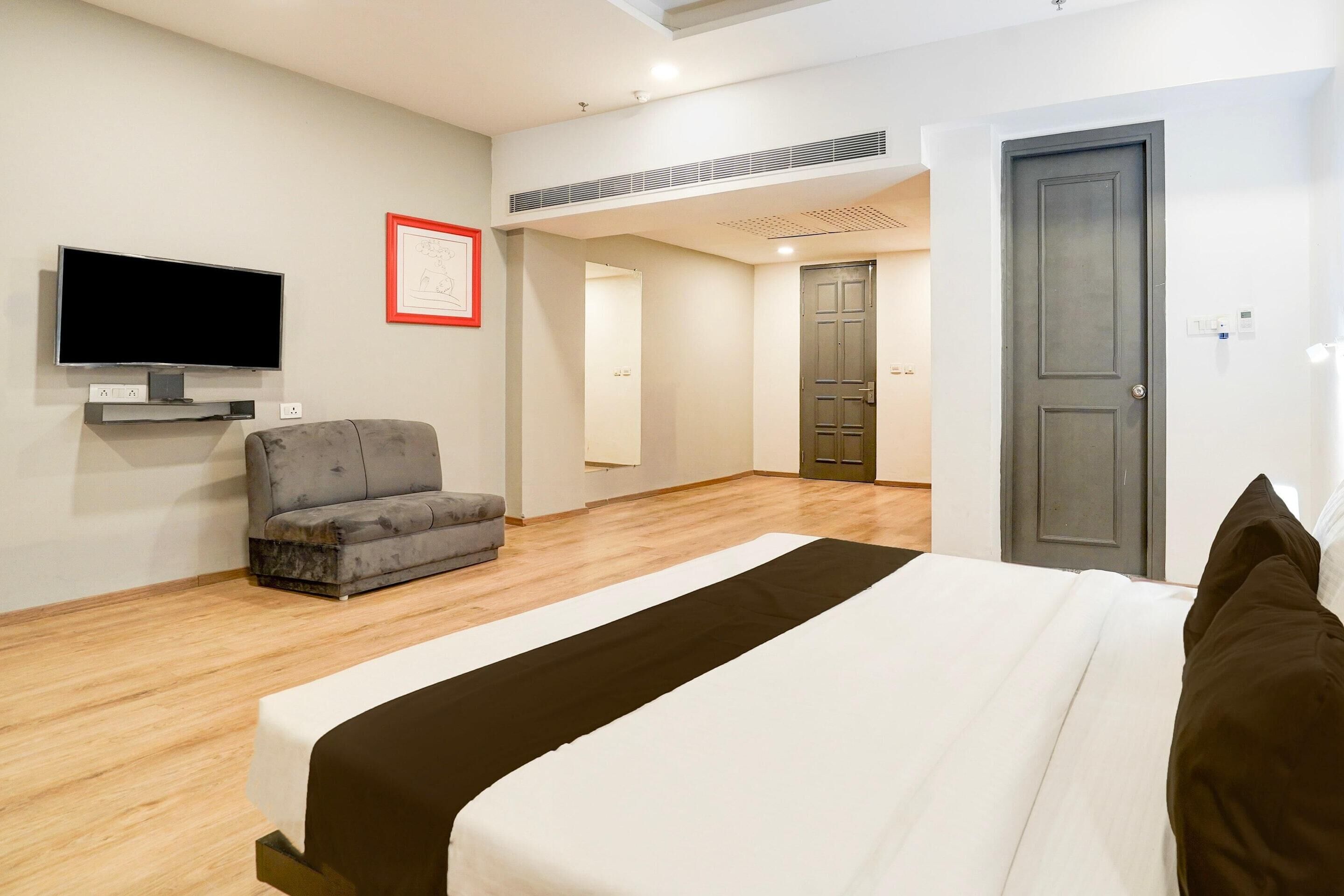 A hotel room with a bed, a flat-screen TV, a sofa, and a door.