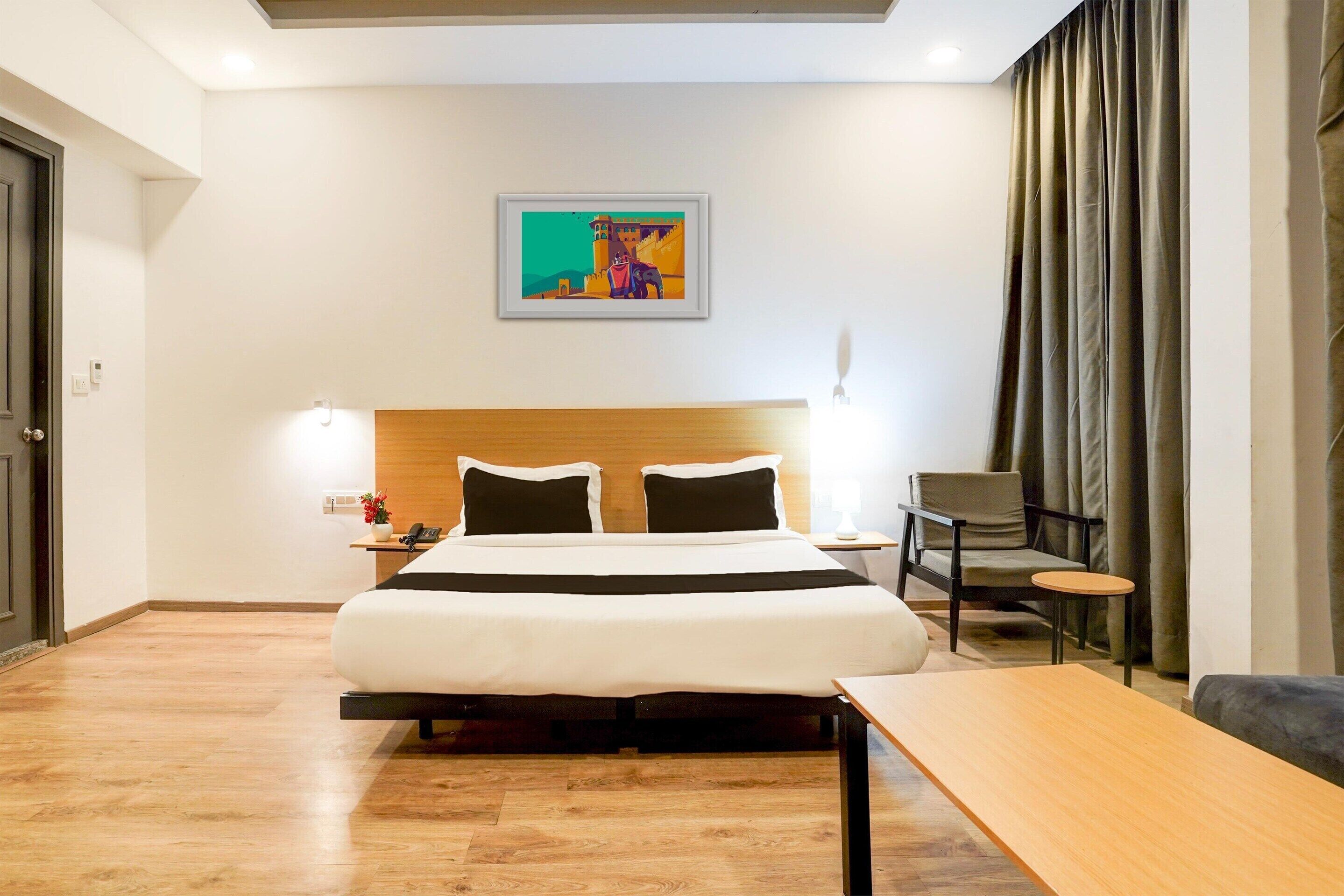 Una habitación de hotel con cama, mesita de noche, silla y un cuadro en la pared.