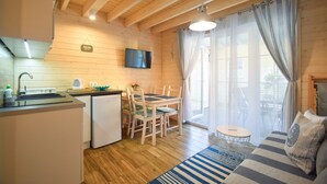 Ein gemütliches Blockhauszimmer mit Holzvertäfelung, einem Essbereich mit Tisch und Stühlen, einer kleinen Küche mit Kühlschrank und einem großen Fenster mit Vorhängen.