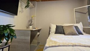 A bedroom with a wooden ceiling, a bed with white bedding, a bedside table, and a plant.