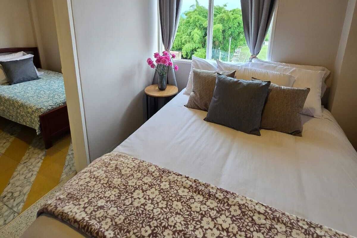 Un dormitorio con cama, mesita de noche, ventana con cortinas y vista a zonas verdes.