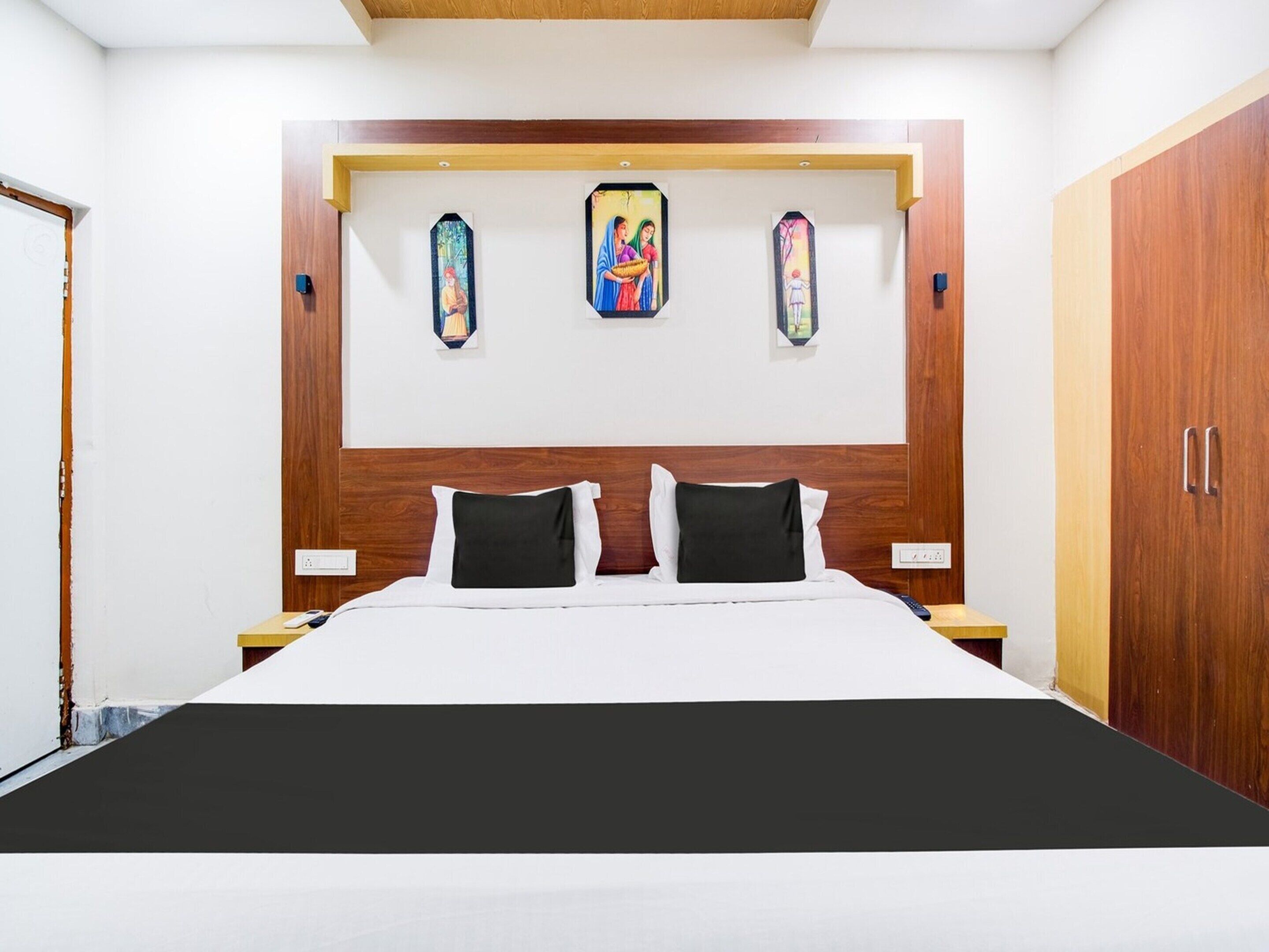 A bedroom with a wooden headboard, a bed with white and black bedding, and three wall-mounted paintings.