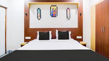 A bedroom with a wooden headboard, a bed with white and black bedding, and three wall-mounted paintings.