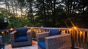 A deck with wicker furniture and string lights. - Cozy authentic log cabin with hot tub, Lake Access, near Sunday River & Mt Abram (Greenwood)