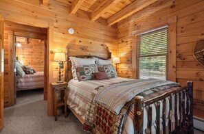 A cozy wooden cabin bedroom with a bed, bedside tables, and a window with blinds.