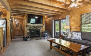 A wooden cabin interior with a fireplace, a television, a sofa, and a ceiling fan.