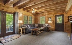 L’intérieur d’une cabane en rondins, avec un ensemble de canapés, deux lampes et un ventilateur de plafond.